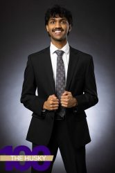 Professional headshot of a person smiling in a suit, with The Husky 100 text