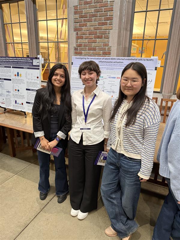 Three young scholars standing in front of research posters indoors