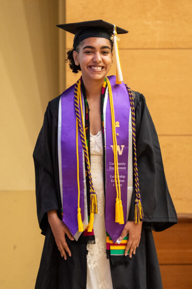 Graduate in cap and gown with honors cords smiling indoors